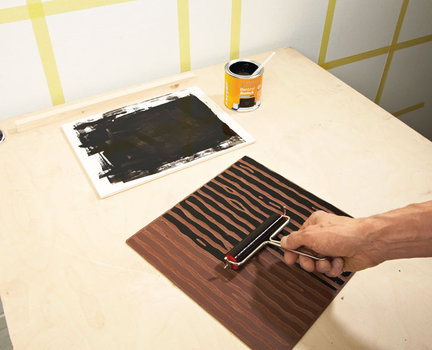 2. Aby na ścianie wykonać wzór, na jej powierzchni wyznaczamy kwadraty i oklejamy ich krawędzie taśmą malarską. Do wyznaczania linii używamy poziomnicy. Następnie na przygotowaną matrycę z linoleum nakładamy wałkiem malarskim warstwę czarnej farby akrylowej.